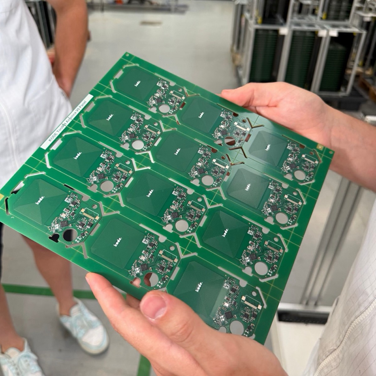 First assembled Kode Dot antenna PCB panel, 12 boards in a 4x3 grid, held in two hands at the factory