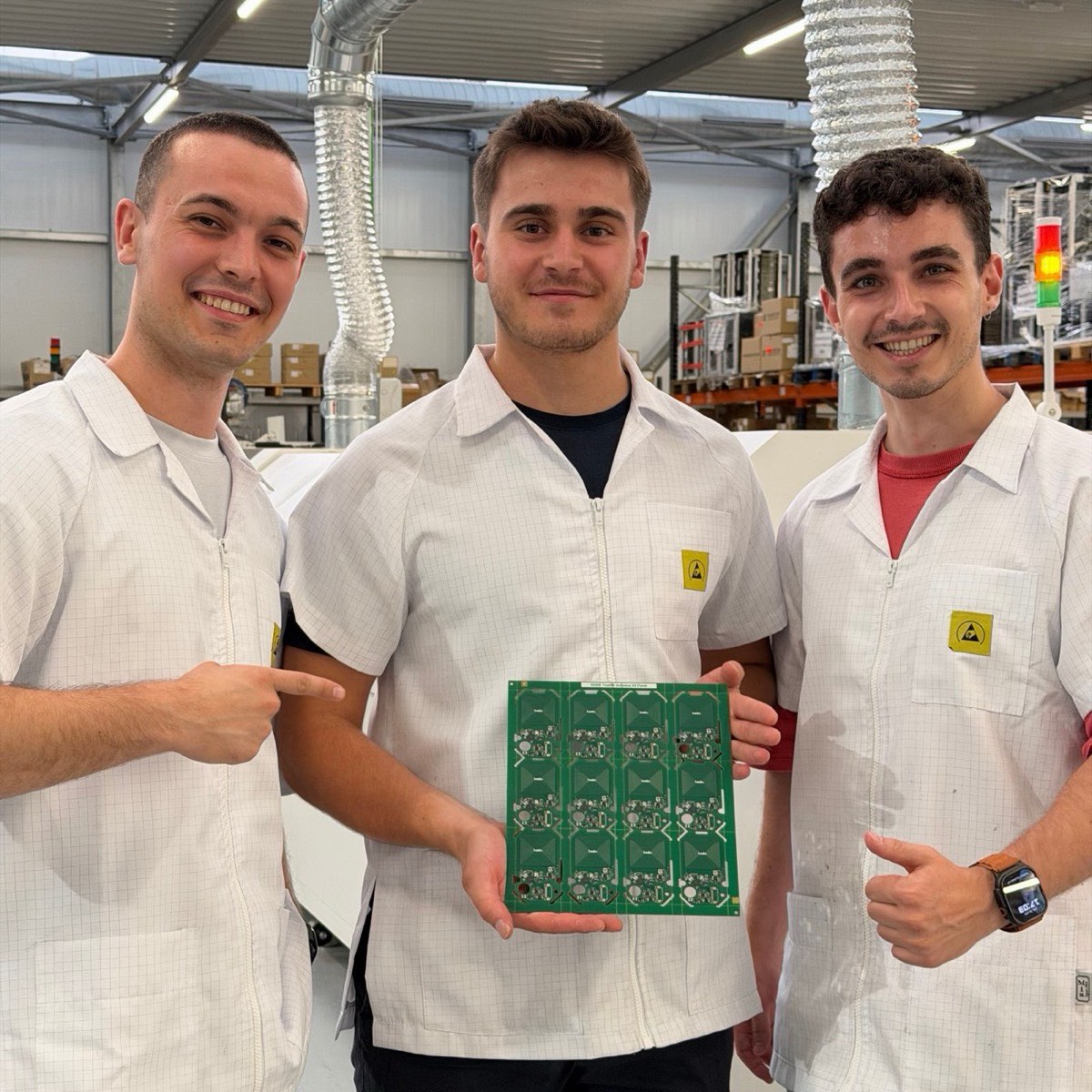 Three engineers in ESD coats at the assembly line holding the first assembled Kode Dot antenna panel