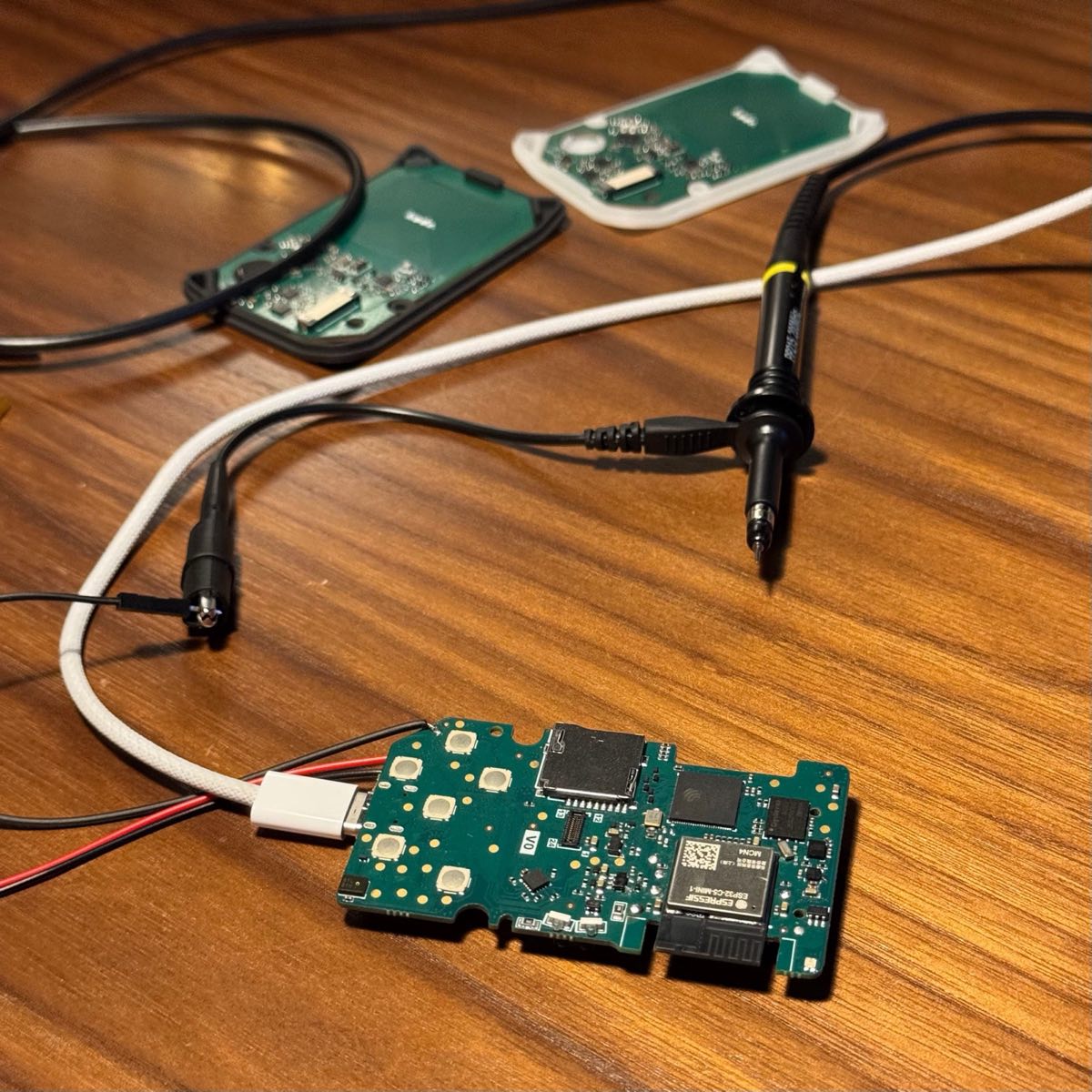 Assembled Kode Dot main PCB wired to power and oscilloscope probes on the bench, with two more boards in enclosure halves behind